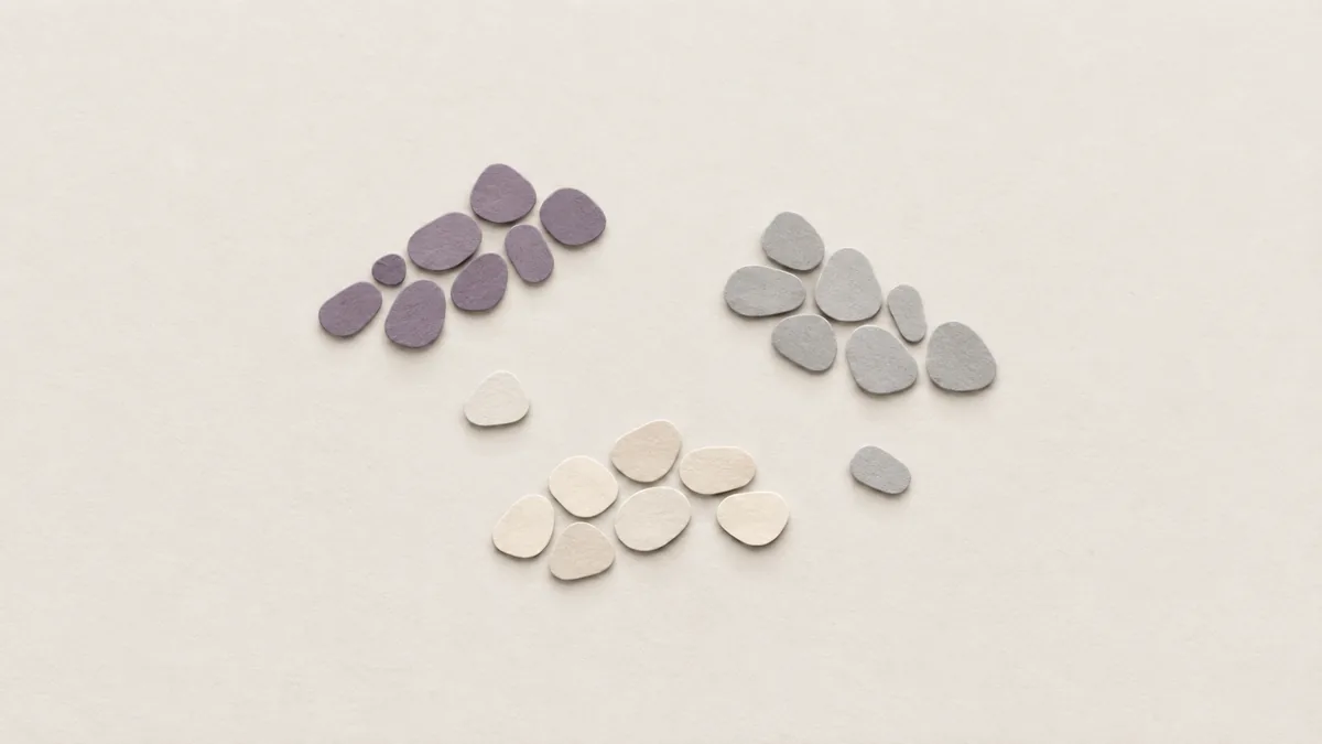 Small paper pebbles on off-white paper, gathered into three loose clumps, one clump violet.